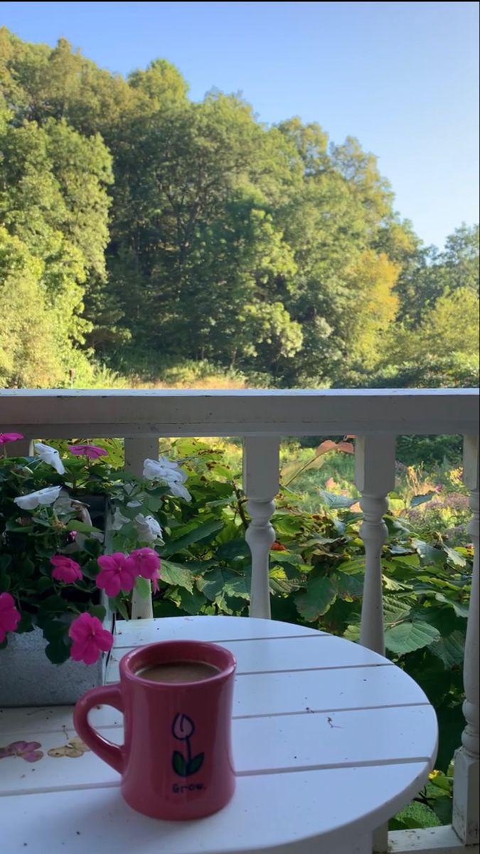 a cup of coffee sitting on top of a white table next to pink and white flowers