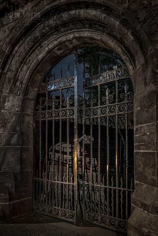 an iron gate in front of a stone building at night with the moon behind it