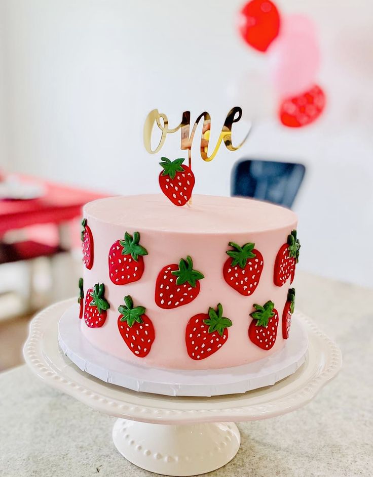 a pink cake with strawberries and the number one on top is sitting on a table