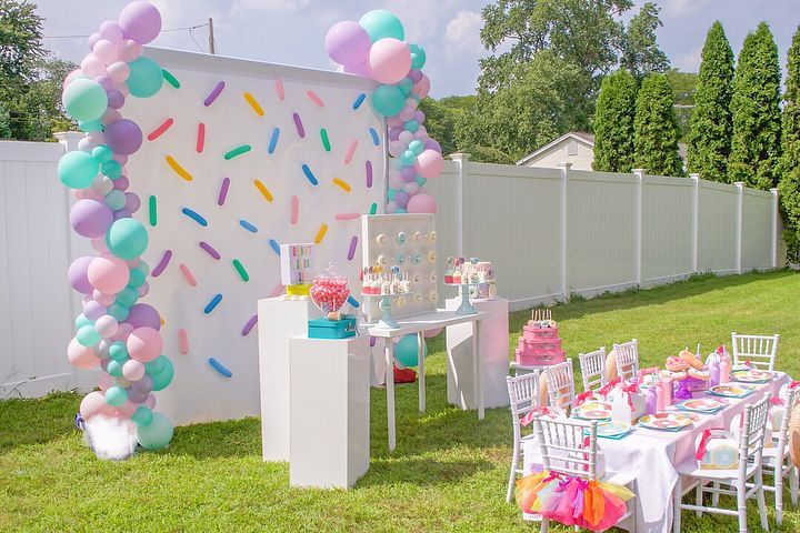 an outdoor party with balloons, cake and confetti on the wall behind it