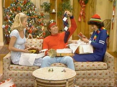 two women and a man sitting on a couch in front of a christmas tree with presents