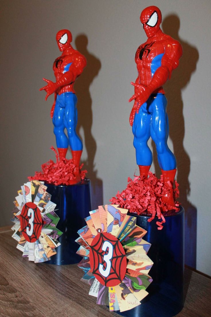 two spider - man figurines are on display in front of a wall and table