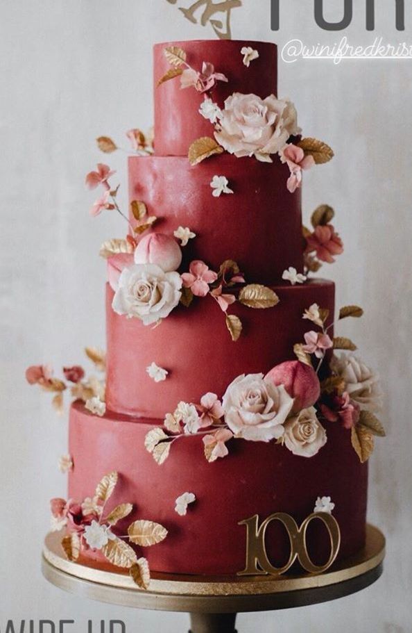 a three tiered red wedding cake with pink flowers on the top and gold lettering