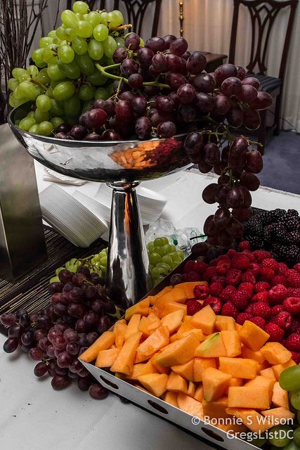 grapes, raspberries, and other fruits are arranged on a table with silver trays