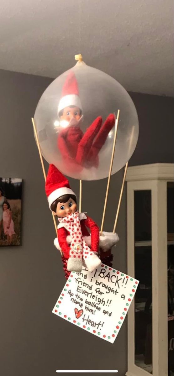 an elf with a sign attached to it's back hanging from a balloon in the air