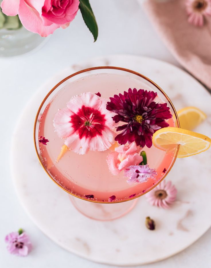 a pink drink with flowers in it on a white plate next to a flower vase