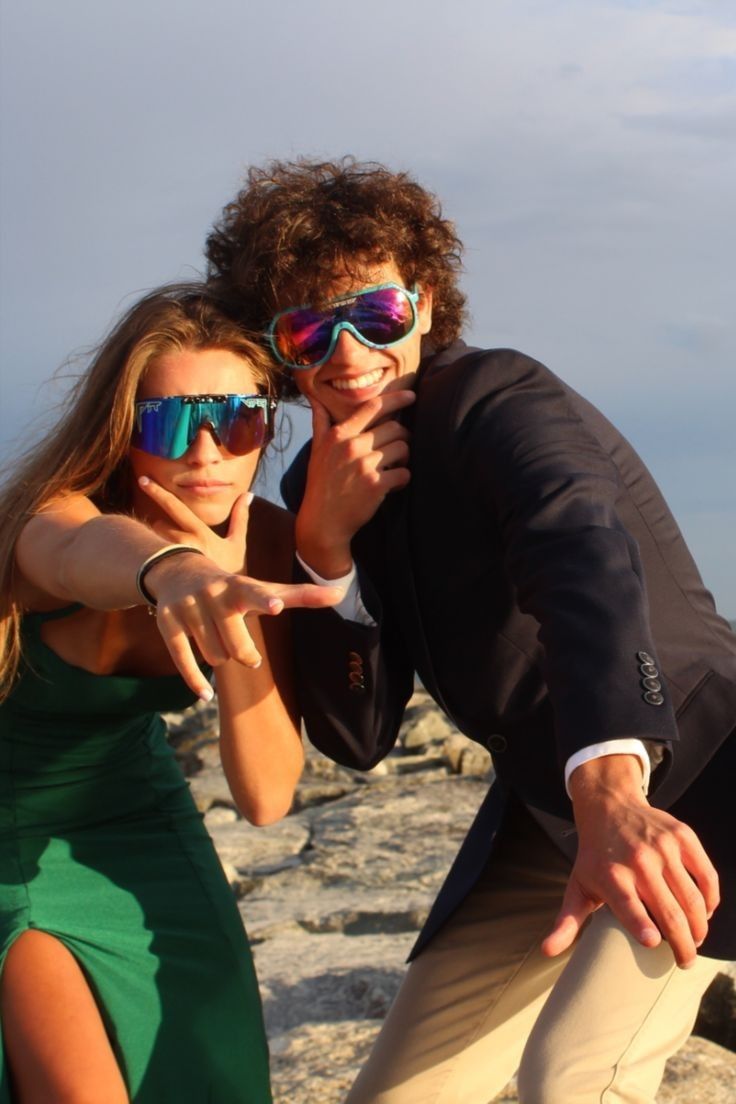 the man and woman are posing for a photo on the rocky beach with their arms around each other