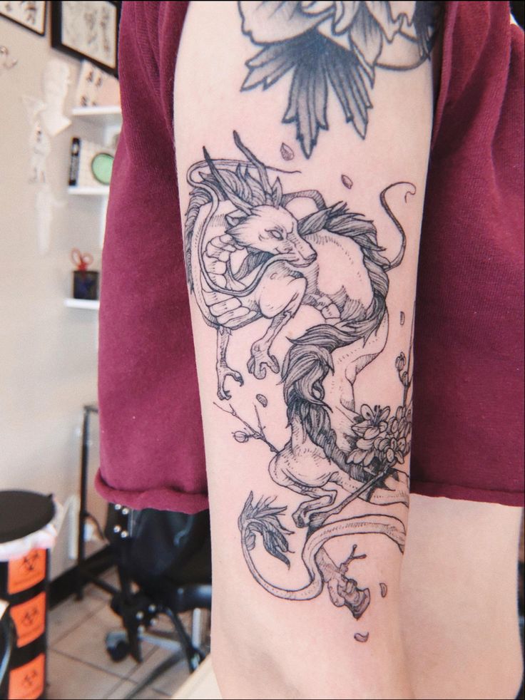 a woman's arm with a tattoo on it and flowers in the corner behind her