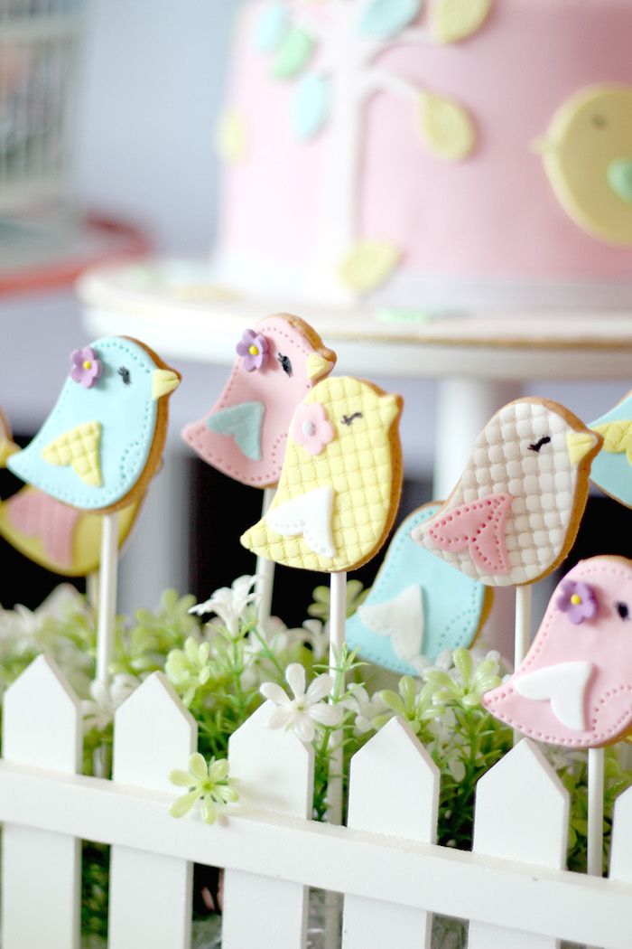 there are many decorated birds on the sticks in front of some cake and cupcakes