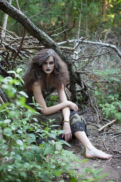 a woman is sitting on the ground in the woods with her hair blowing in the wind