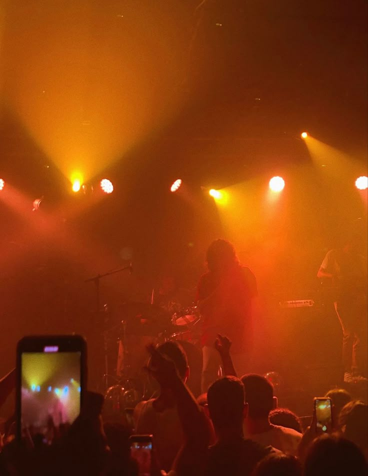 a concert scene with people on the stage and one person holding up a cell phone