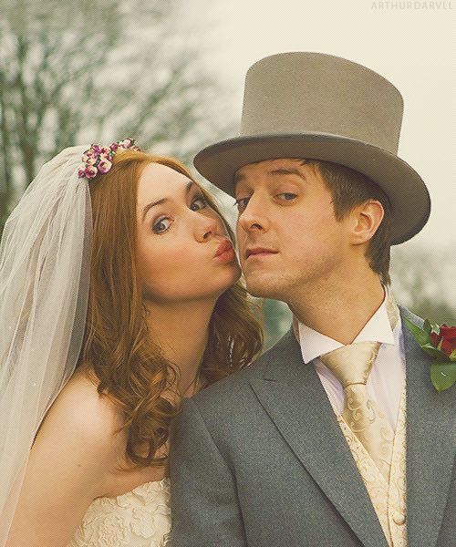 a man and woman dressed in wedding attire kissing each other with a hat on their head