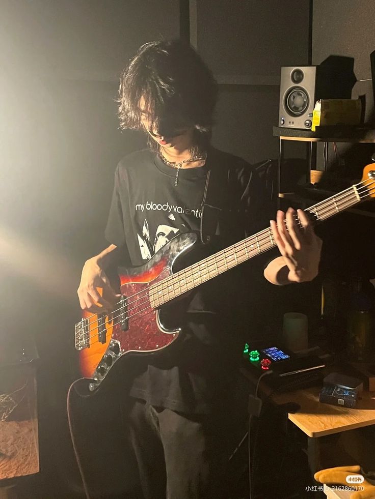 a young man playing an electric bass guitar in a dimly lit room with sound equipment