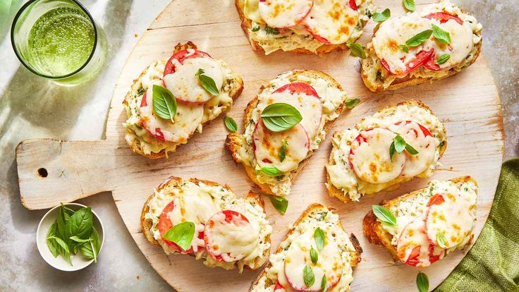 small sandwiches with cheese and vegetables on a cutting board next to a glass of green juice