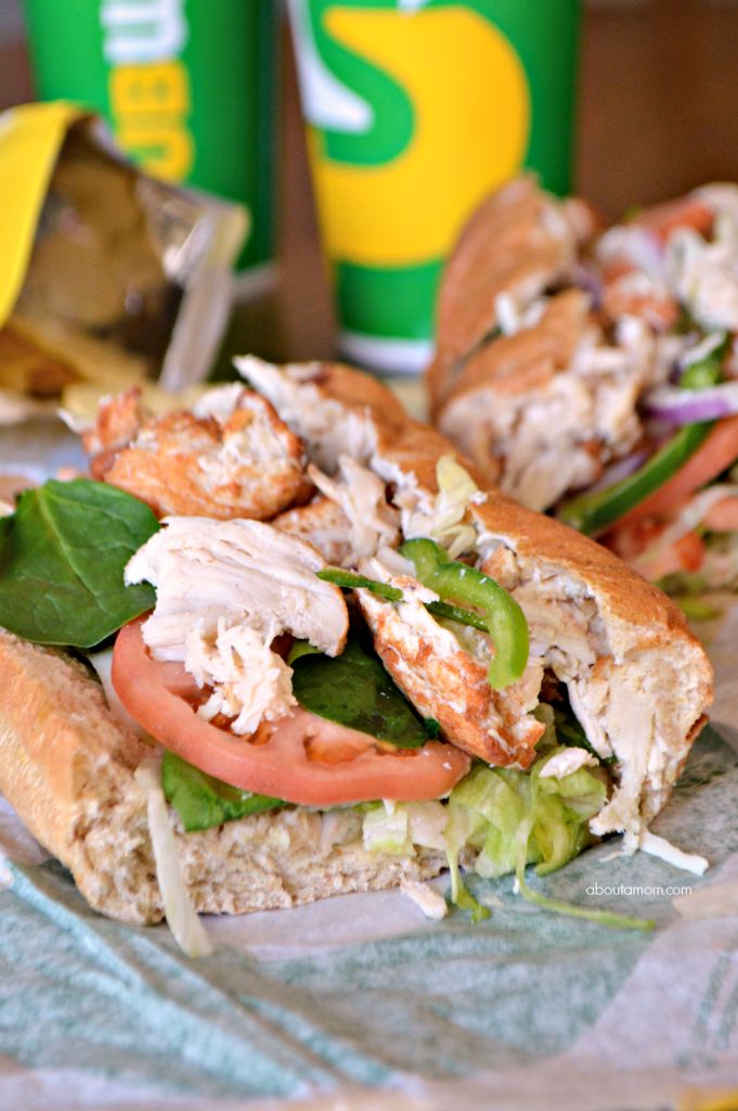 a sandwich with chicken, lettuce and tomatoes on it next to two soft drinks