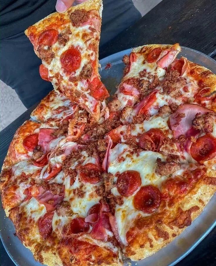 a pizza with pepperoni and sausage cut into slices on a metal platter, ready to be eaten