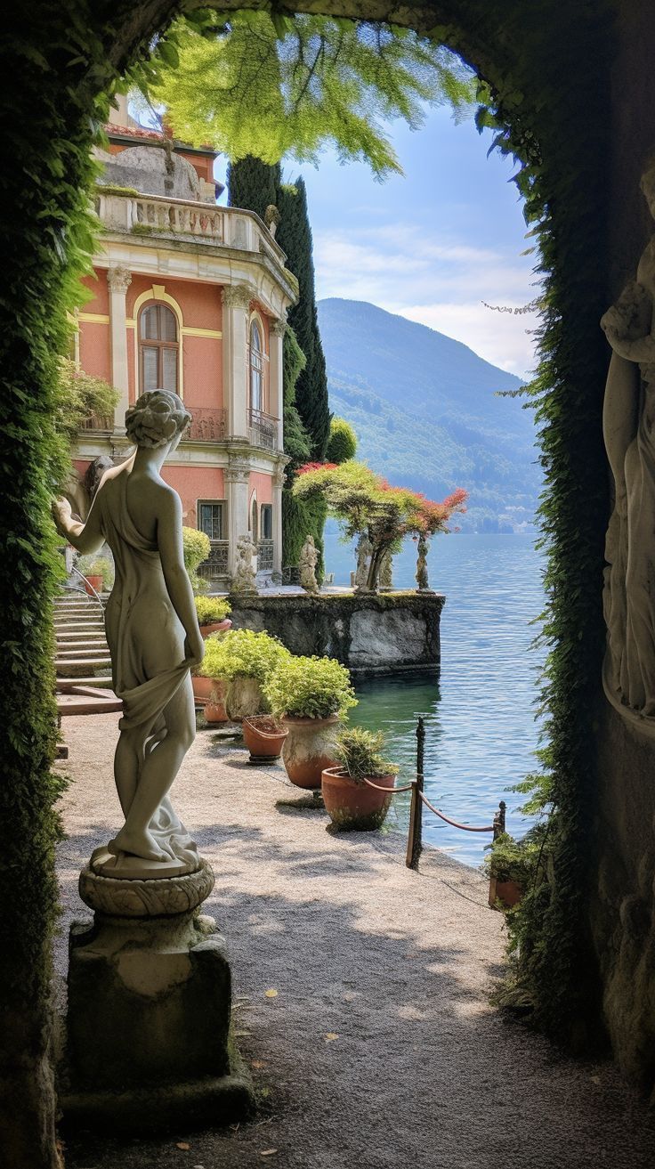 a statue is in the middle of an archway leading to a building with a lake and mountains in the background