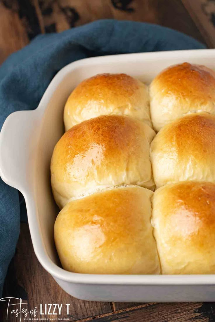 a white casserole dish filled with rolls on top of a blue cloth next to a wooden table