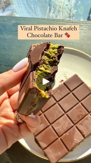 a person holding a piece of chocolate on top of a white plate with green toppings