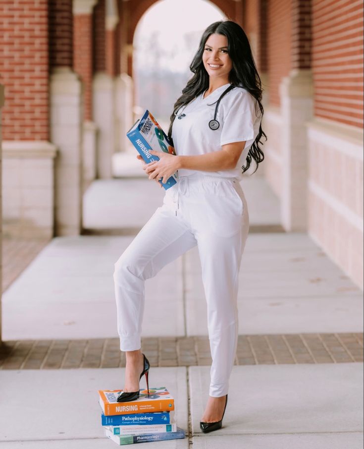 a woman in white jumpsuits holding a book and posing for the camera with her hands on her hips