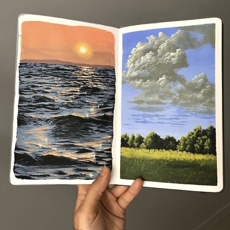 a hand holding an open book with water and clouds