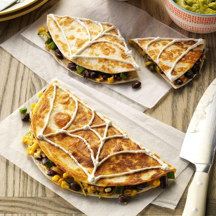 two quesadillas with black beans, corn and cheese on parchment paper next to a knife