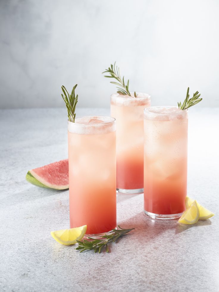 three glasses filled with watermelon lemonade and rosemary garnish on a table