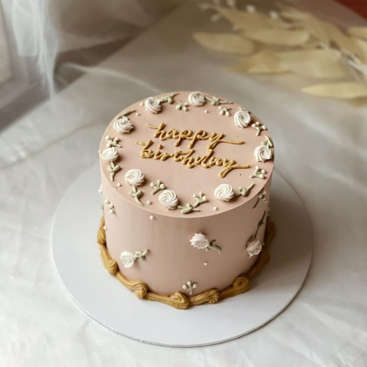 a pink birthday cake sitting on top of a white tablecloth covered table with flowers