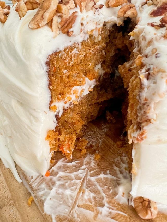 a carrot cake with white frosting and chopped nuts on top is cut in half