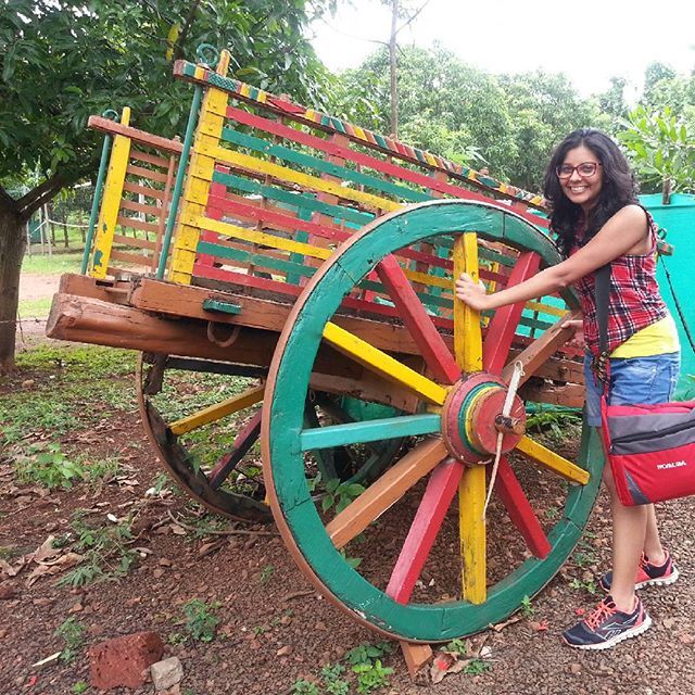 a woman standing next to a colorful wooden cart with wheels on the side and trees in the background