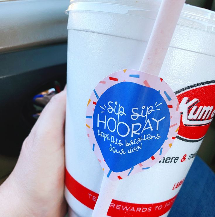 a hand holding a cup with a straw in it and a sticker that says sip stop hooray