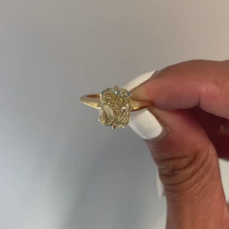 a woman's hand holding an engagement ring with a yellow diamond in the center