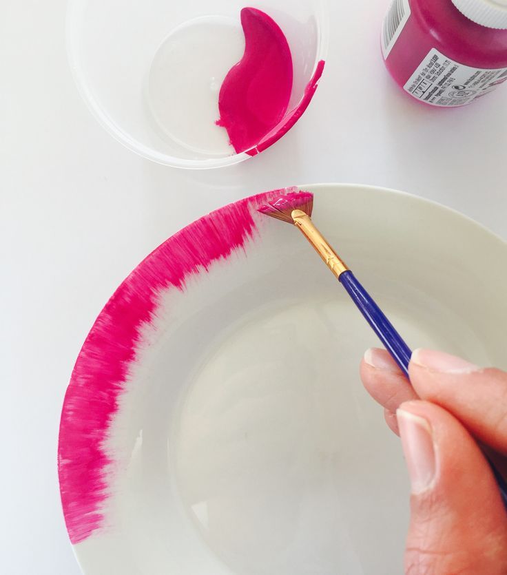 a person holding a paintbrush in front of a white plate with pink and red paints on it