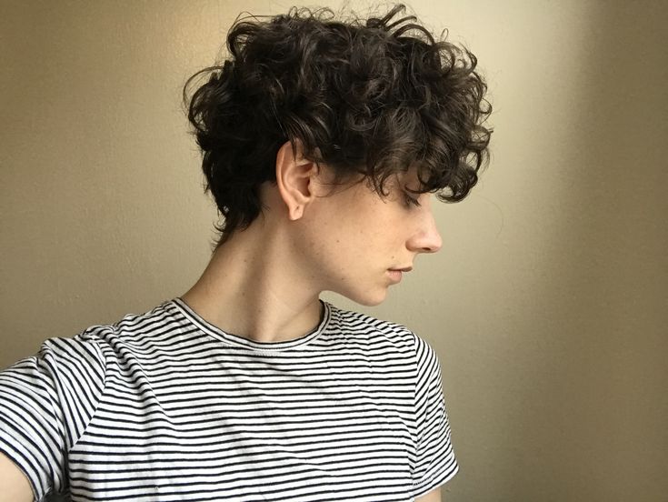 a young man with curly hair wearing a striped t - shirt looking off to the side