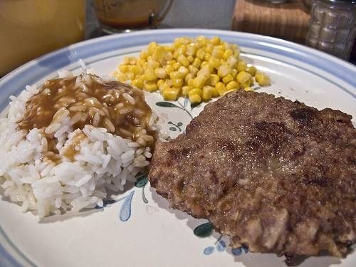 the meal is prepared and ready to be eaten on the plate, including rice, corn, and meat