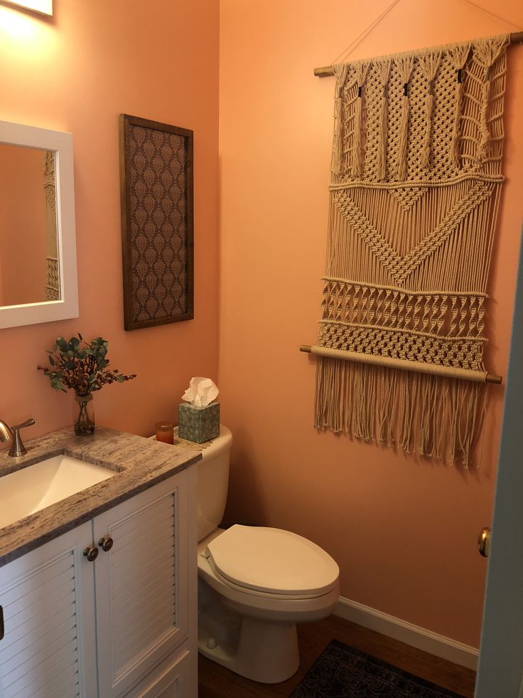 a white toilet sitting next to a sink in a bathroom under a hanging wall decoration