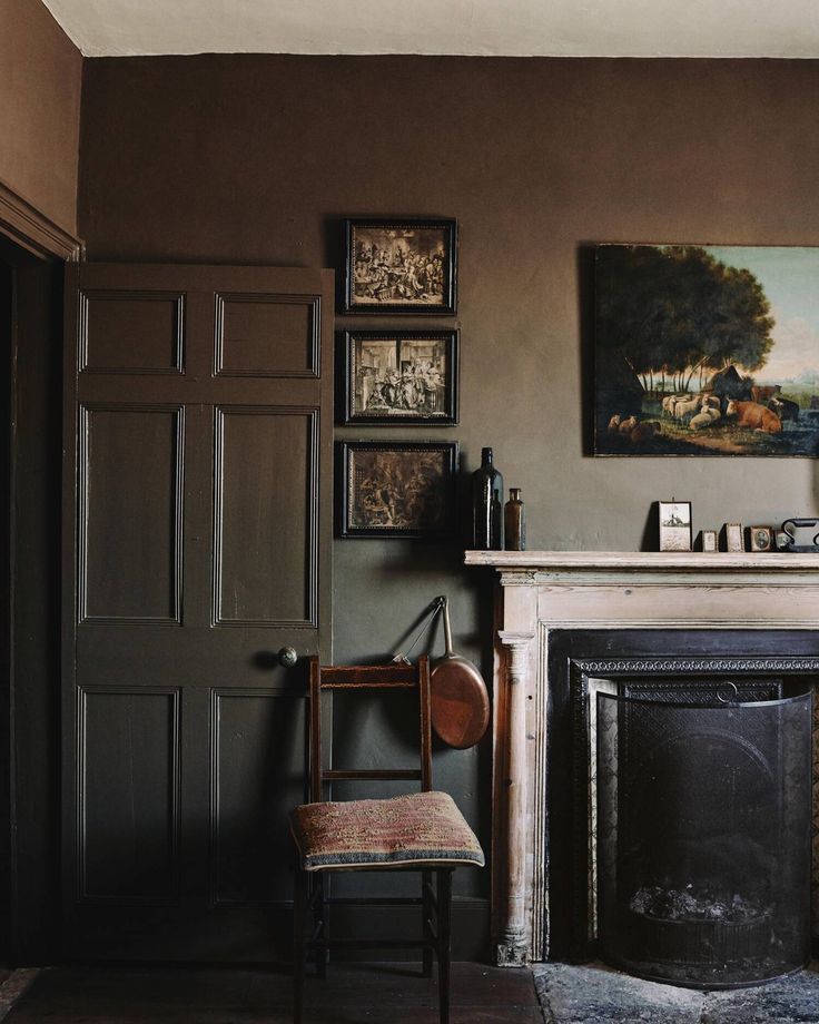 a chair sitting in front of a fireplace with pictures on the wall and paintings above it