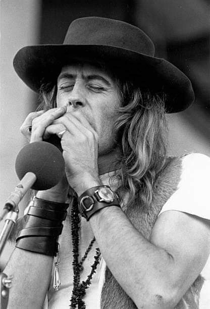 a man with long hair wearing a hat and holding a microphone