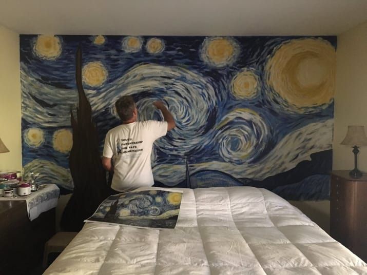 a man standing on top of a bed in front of a starry night mural