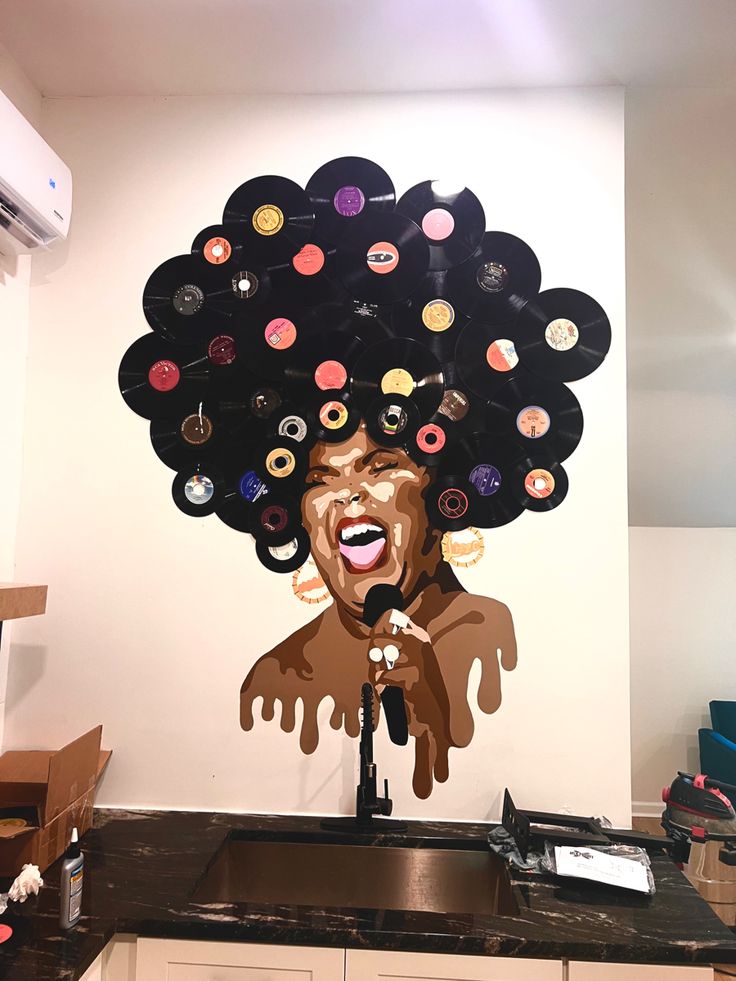 a kitchen area with a sink, counter top and large mural of a woman's face on the wall