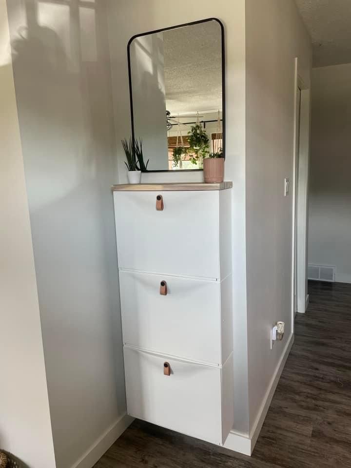 a white cabinet with two drawers and a mirror above it in a room that has hardwood floors