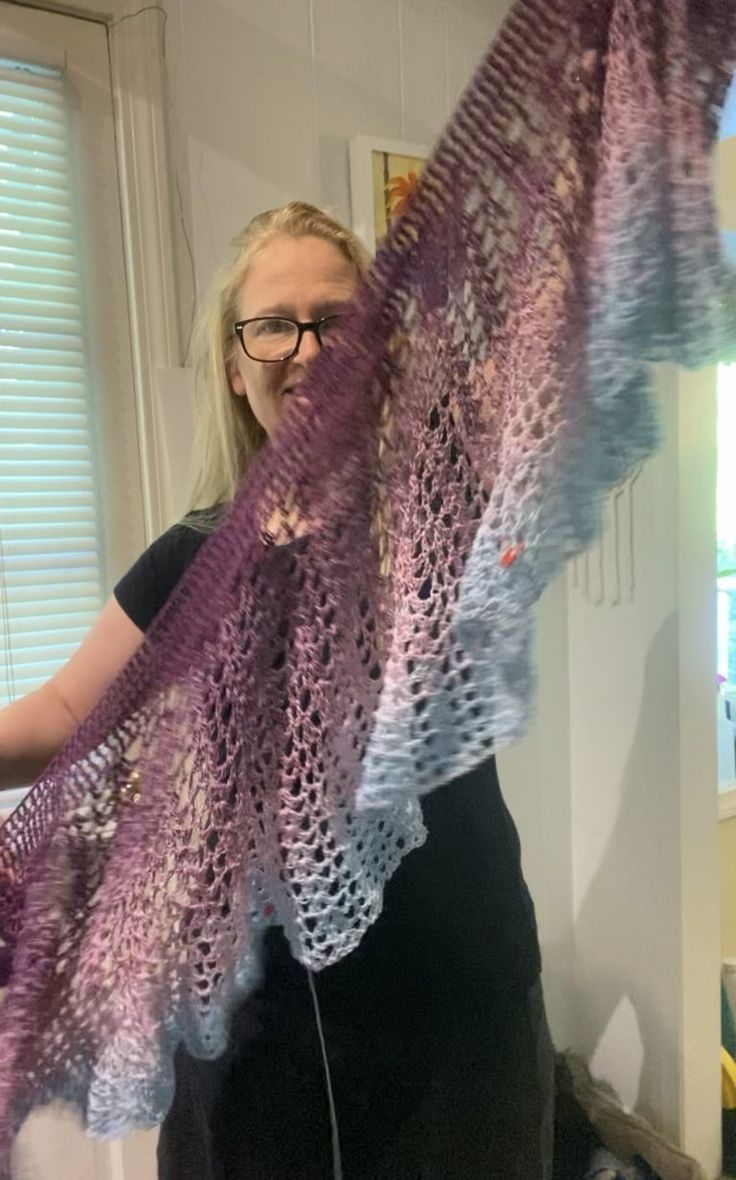 a woman is holding up a purple shawl