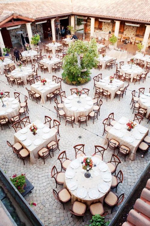 an outdoor dining area with tables and chairs set up in the center, surrounded by greenery