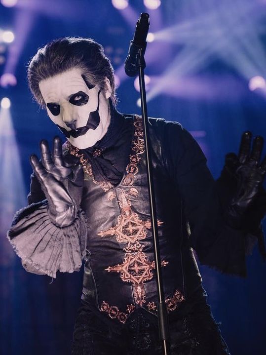 a man wearing a mask and holding a microphone in front of his face on stage