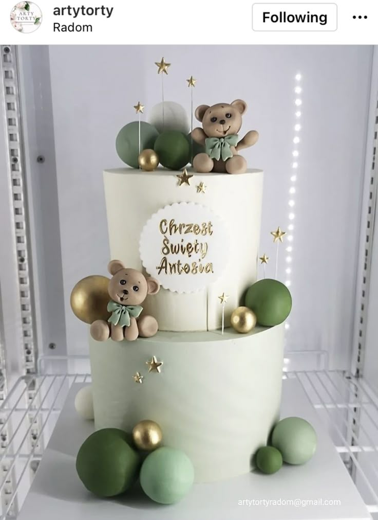 a white cake with green and gold decorations on the bottom tier, topped with teddy bears