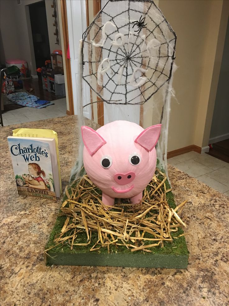 a pink pig sitting on top of a pile of hay next to a book