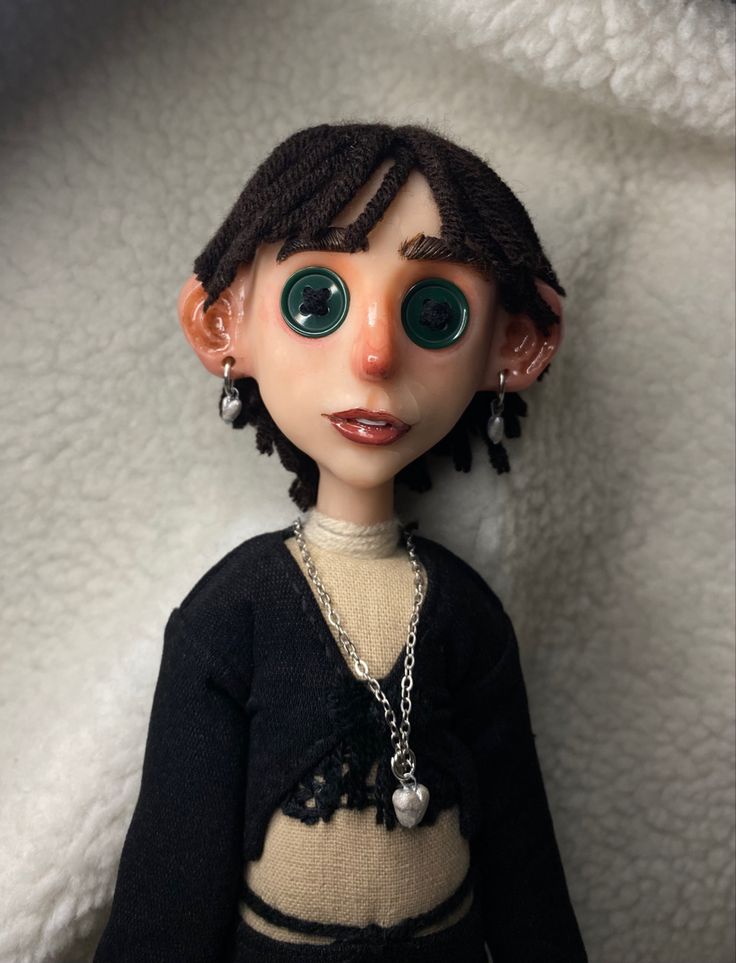 a doll with green eyes wearing a black sweater and silver chain around it's neck