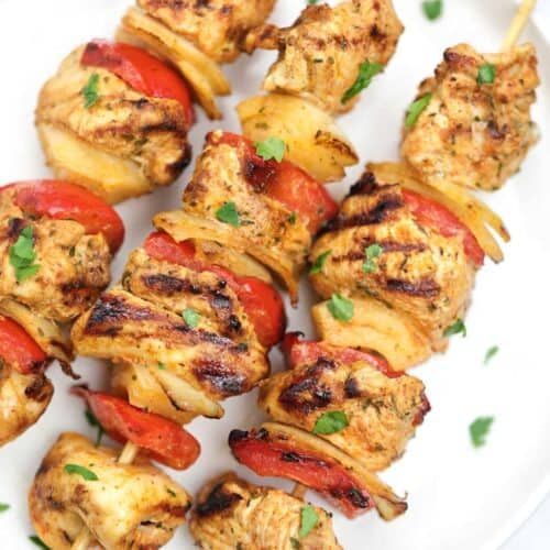 chicken kabobs on skewers with peppers and onions served on a white plate