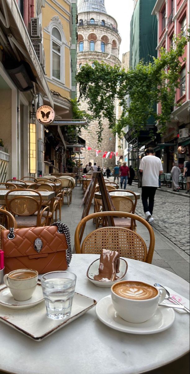 the table is set with two cups of coffee and an orange handbag on it