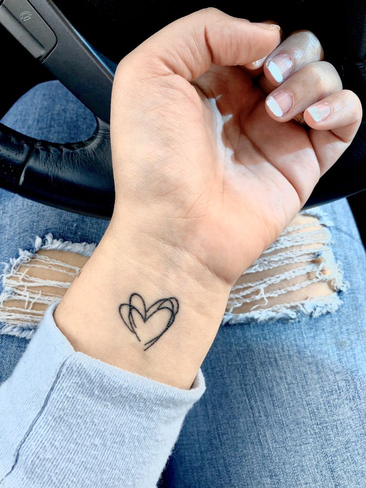 a woman's wrist with a small heart tattoo on the left side of her arm